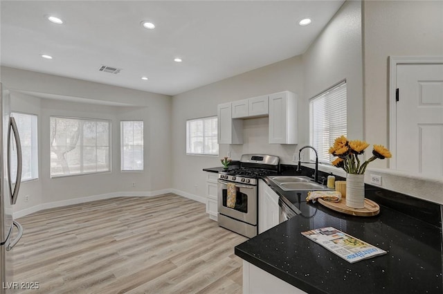 kitchen with dark countertops, appliances with stainless steel finishes, light wood-type flooring, white cabinetry, and recessed lighting