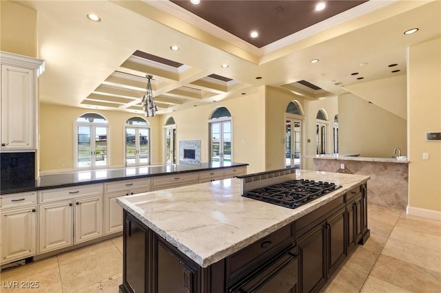 kitchen featuring coffered ceiling, a kitchen island, open floor plan, dark stone countertops, and gas stovetop