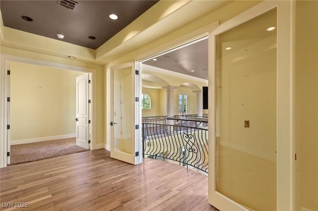 hallway with ornate columns, arched walkways, a raised ceiling, and wood finished floors