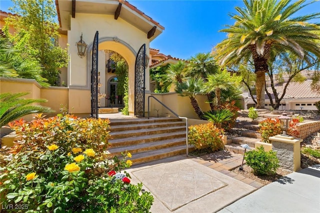 view of exterior entry featuring a tiled roof, fence, and stucco siding