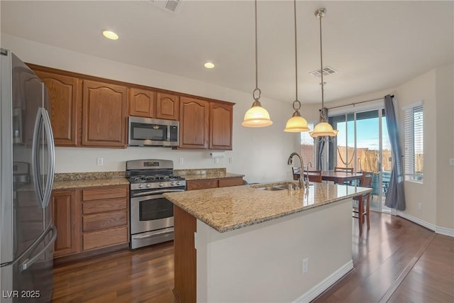 kitchen with a sink, light stone countertops, brown cabinets, appliances with stainless steel finishes, and dark wood-style flooring