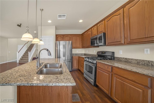 kitchen featuring visible vents, light stone counters, brown cabinetry, stainless steel appliances, and a sink