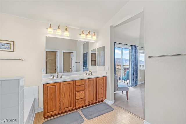 bathroom with baseboards, a sink, double vanity, and a bathing tub