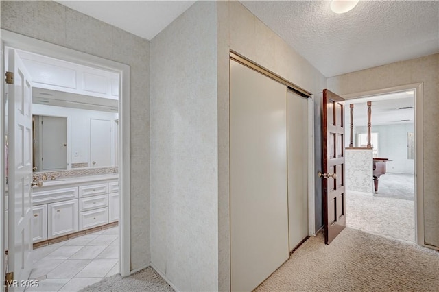 hall with light tile patterned floors, a textured ceiling, a sink, and light colored carpet