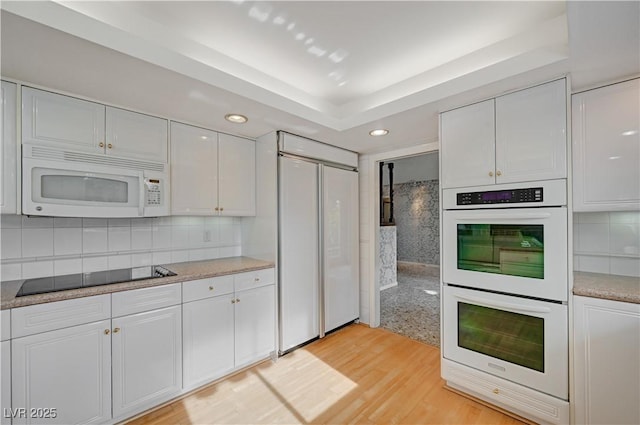 kitchen with white appliances, tasteful backsplash, a raised ceiling, light wood-style floors, and white cabinetry