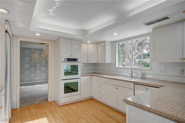 kitchen featuring visible vents, white cabinetry, a sink, light wood-type flooring, and white appliances