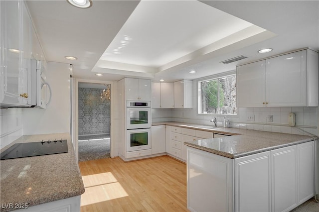 kitchen featuring a raised ceiling, light wood-style flooring, decorative backsplash, white cabinets, and white appliances