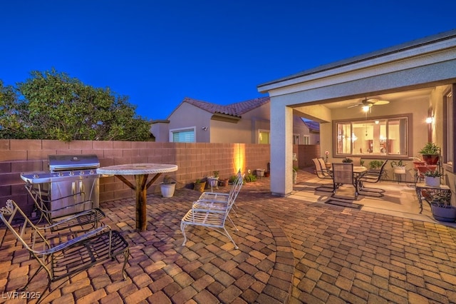 patio at night featuring ceiling fan, outdoor dining space, fence, and a grill