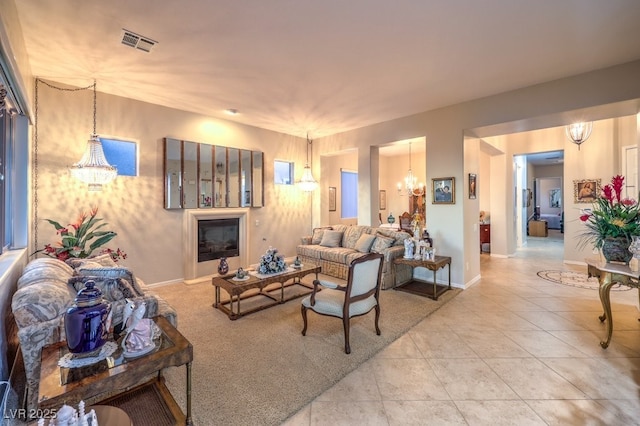 living room featuring baseboards, visible vents, a glass covered fireplace, tile patterned flooring, and a notable chandelier