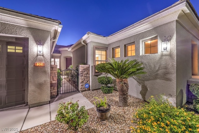 entrance to property with a garage, a gate, and stucco siding