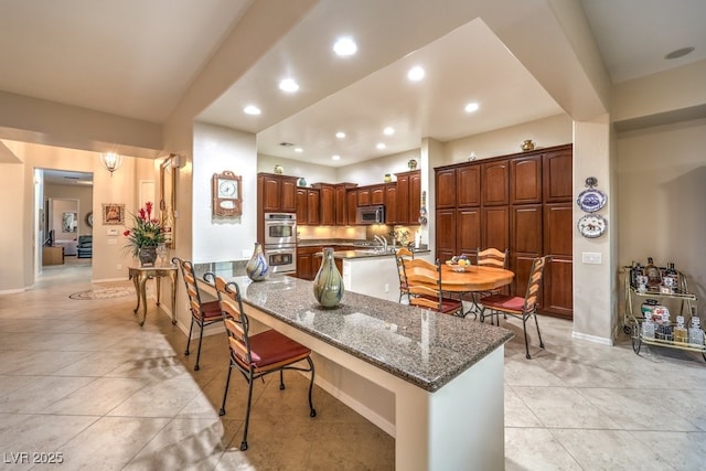 kitchen with light tile patterned floors, recessed lighting, a breakfast bar, appliances with stainless steel finishes, and dark stone counters