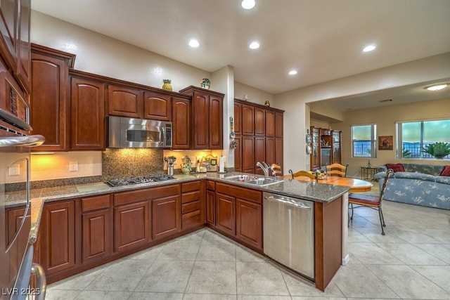 kitchen featuring dark stone counters, open floor plan, a peninsula, stainless steel appliances, and a sink