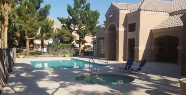 community pool with a patio area, fence, and a hot tub