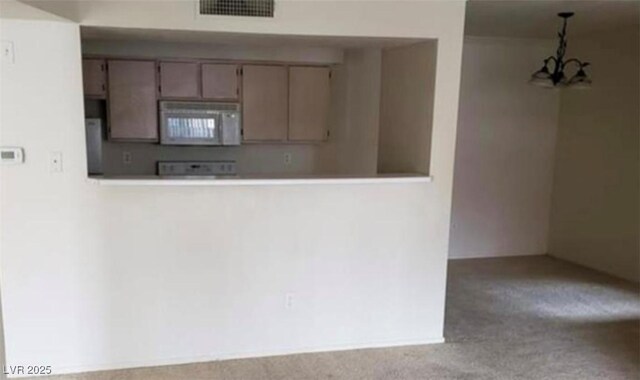 kitchen featuring a chandelier, white microwave, carpet floors, visible vents, and decorative light fixtures