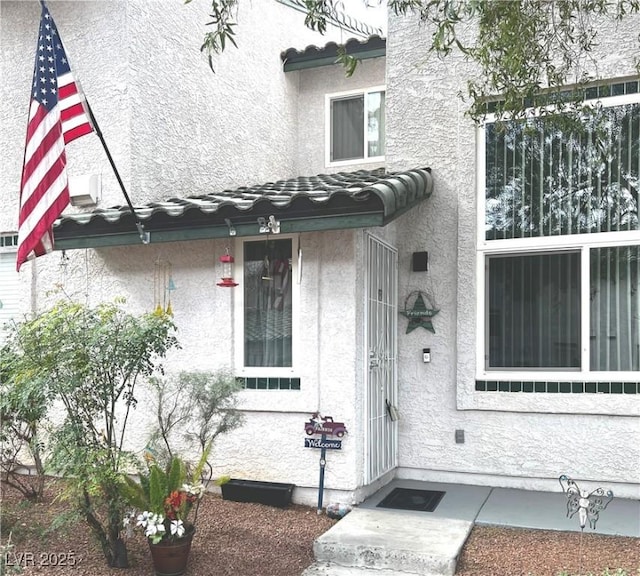 view of exterior entry with a tile roof and stucco siding