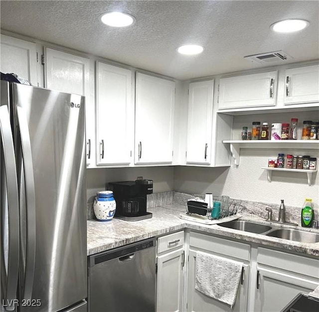 kitchen with appliances with stainless steel finishes, white cabinetry, a sink, and a textured ceiling