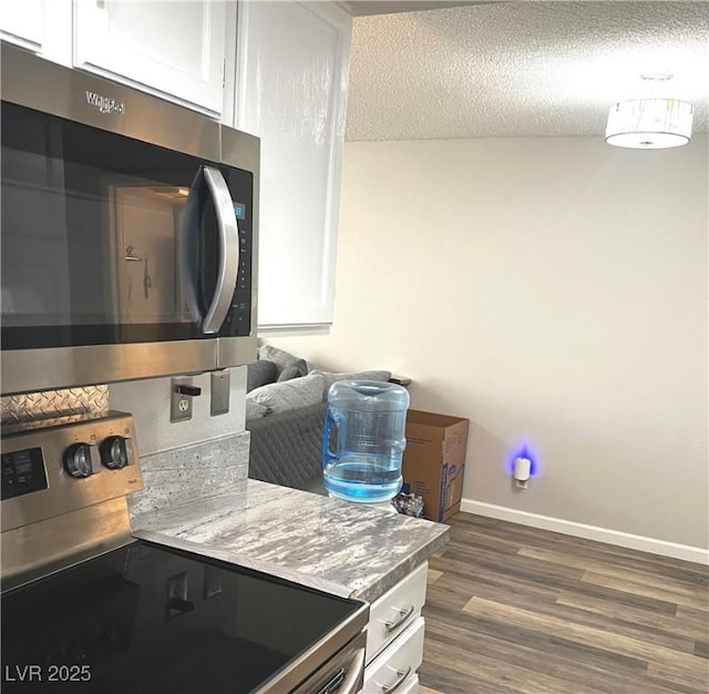 kitchen featuring dark wood-type flooring, appliances with stainless steel finishes, white cabinets, and a textured ceiling