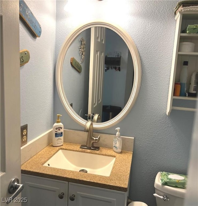 half bath with toilet, a textured wall, and vanity