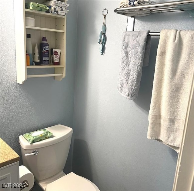 bathroom with a textured wall, vanity, and toilet