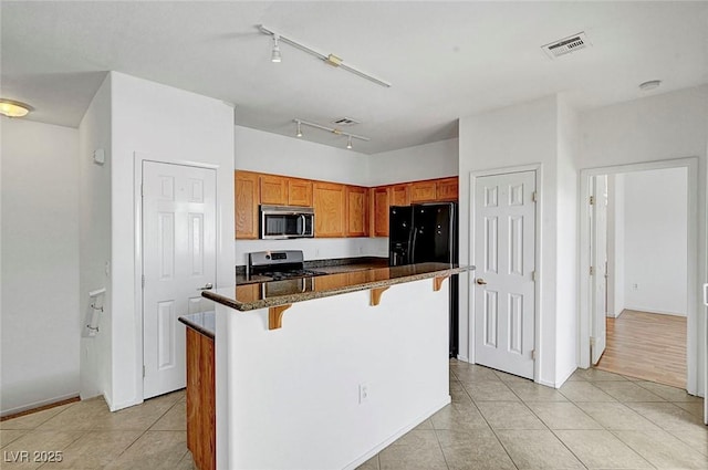 4020 Smokey Fog Ave Unit 201, North Las Vegas, NV 89081 - kitchen with appliances with stainless steel finishes, a breakfast bar, light tile patterned floors, dark stone countertops, and brown cabinets