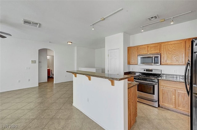 4020 Smokey Fog Ave Unit 201, North Las Vegas, NV 89081 - kitchen featuring appliances with stainless steel finishes, a breakfast bar, track lighting, arched walkways, and light tile patterned floors