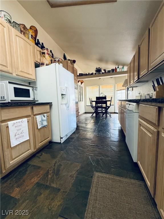 kitchen with white appliances, dark countertops, stone tile flooring, and vaulted ceiling