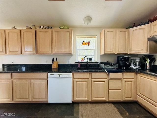 kitchen featuring dark stone counters, a sink, light brown cabinetry, under cabinet range hood, and dishwasher