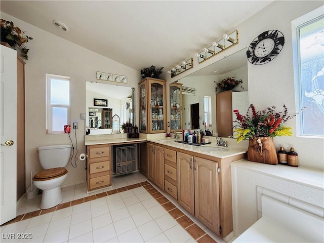 bathroom featuring tile patterned flooring, vaulted ceiling, toilet, a sink, and double vanity