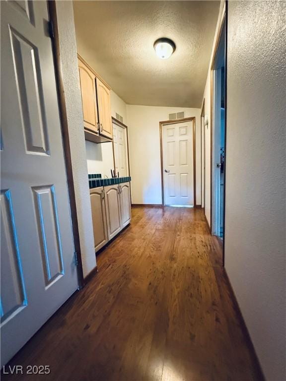 corridor featuring visible vents, a textured ceiling, baseboards, dark wood-style flooring, and a textured wall