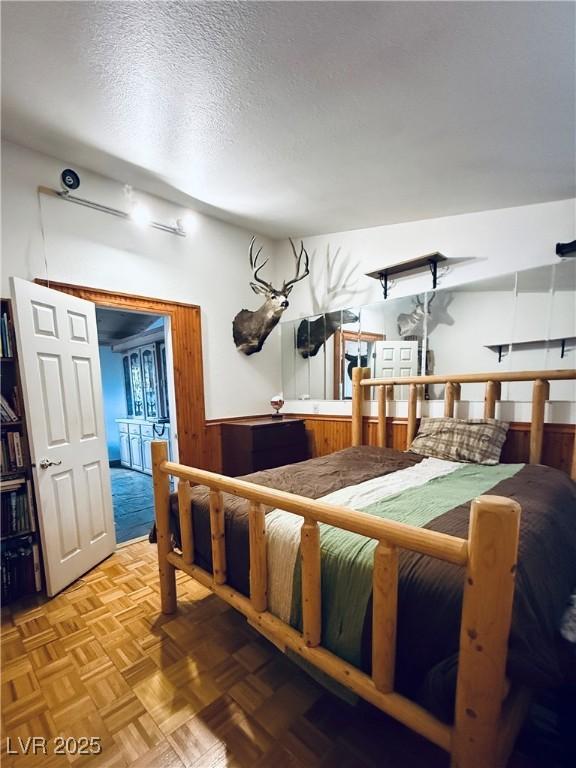 bedroom featuring wainscoting, wood walls, and a textured ceiling