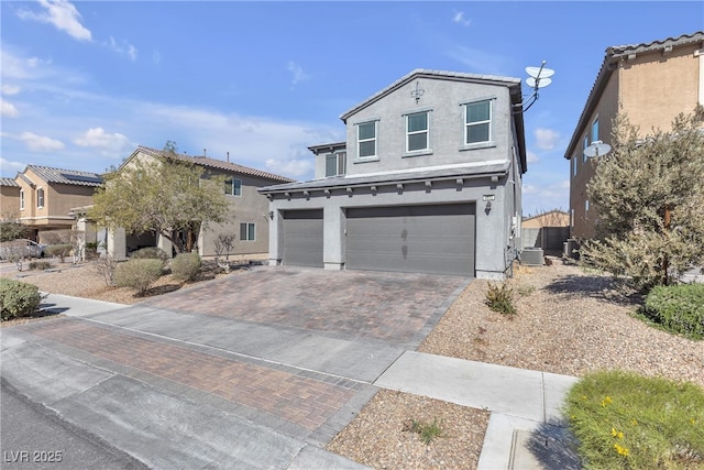 traditional-style home featuring decorative driveway, a garage, central AC, and stucco siding