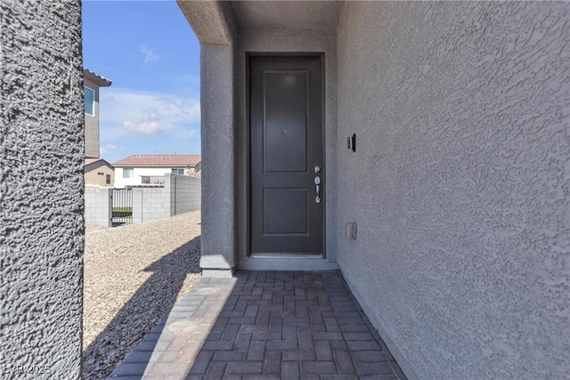 entrance to property featuring stucco siding and fence