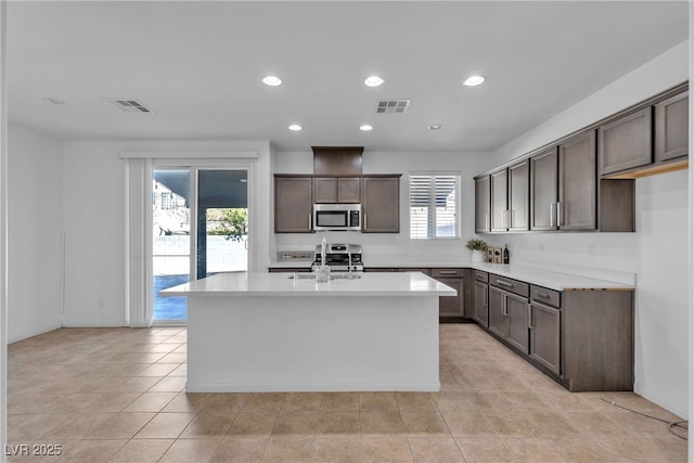 kitchen featuring visible vents, dark brown cabinetry, an island with sink, appliances with stainless steel finishes, and a sink