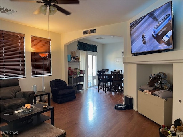 living room featuring a ceiling fan, visible vents, arched walkways, and wood finished floors