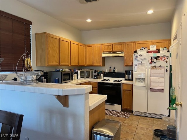 kitchen with tile counters, stainless steel microwave, gas range oven, under cabinet range hood, and white fridge with ice dispenser