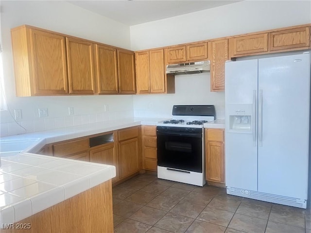 9299 Adamshurst Ave, Las Vegas, NV 89148 - kitchen featuring white fridge with ice dispenser, gas range oven, under cabinet range hood, and tile countertops