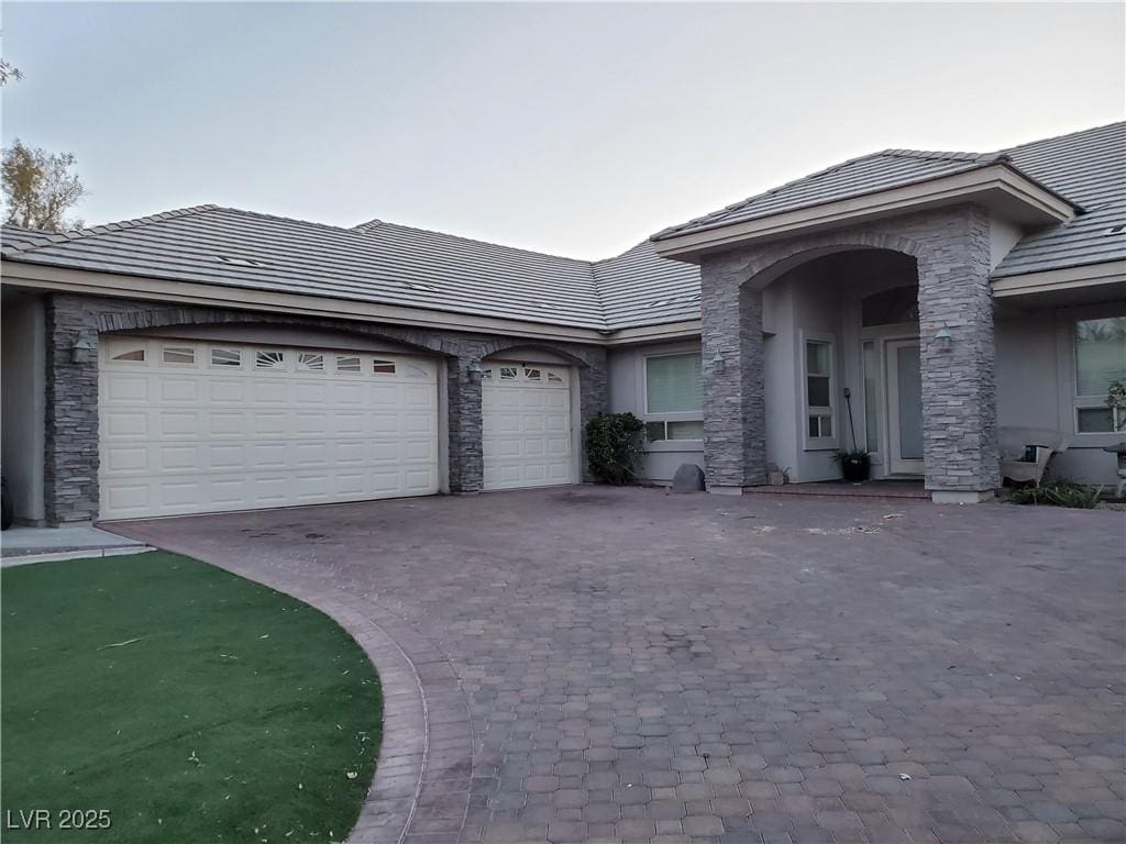 view of front of house with a garage, stone siding, decorative driveway, and stucco siding