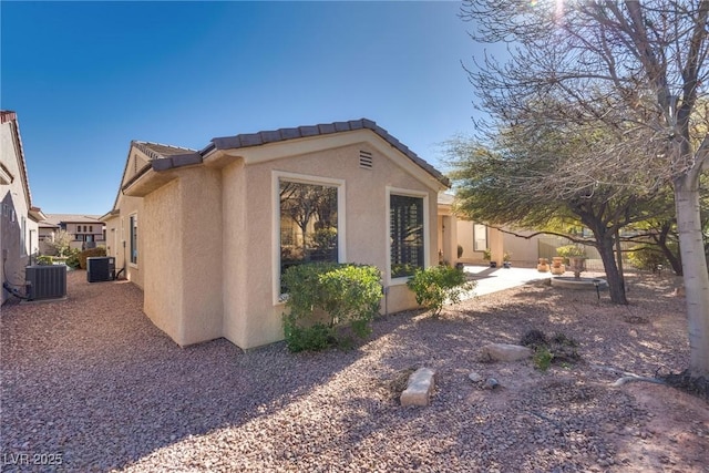 view of side of property featuring a patio area, stucco siding, cooling unit, and a tile roof