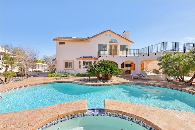 rear view of house featuring a patio, a balcony, a pool with connected hot tub, stucco siding, and a chimney