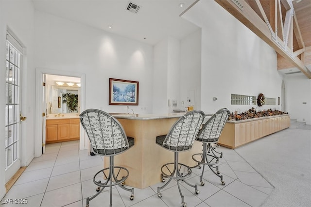 kitchen with a breakfast bar, light tile patterned floors, visible vents, a high ceiling, and light brown cabinets