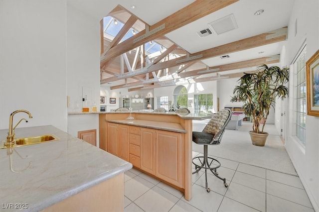 kitchen featuring visible vents, open floor plan, beamed ceiling, light brown cabinets, and a sink