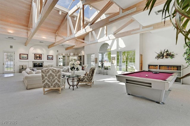 playroom with high vaulted ceiling, carpet floors, a skylight, beamed ceiling, and a glass covered fireplace