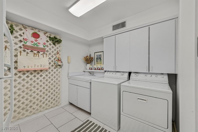 laundry area featuring light tile patterned floors, separate washer and dryer, a sink, visible vents, and cabinet space