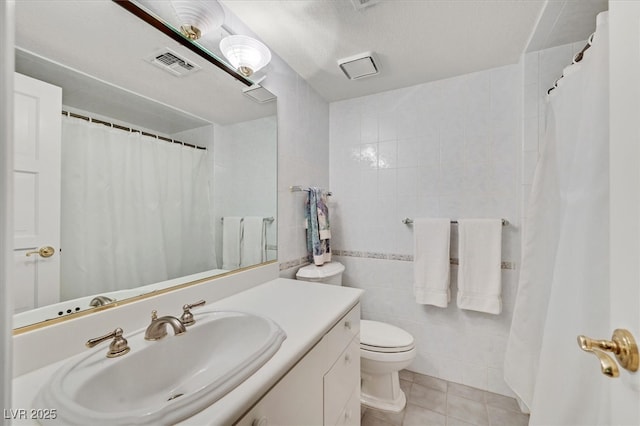 full bath with visible vents, toilet, tile patterned floors, vanity, and tile walls