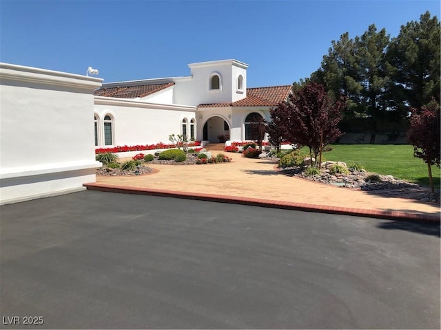 mediterranean / spanish home featuring a front yard, a tile roof, and stucco siding