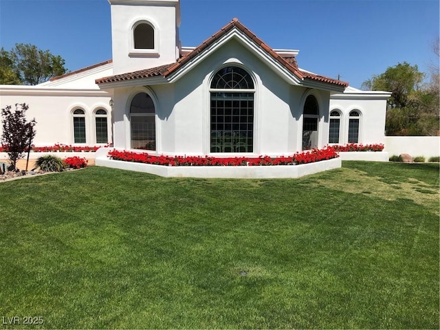 rear view of property featuring a yard, a tiled roof, and stucco siding