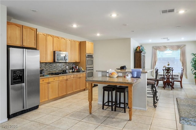 kitchen featuring light tile patterned floors, visible vents, decorative backsplash, appliances with stainless steel finishes, and a breakfast bar area