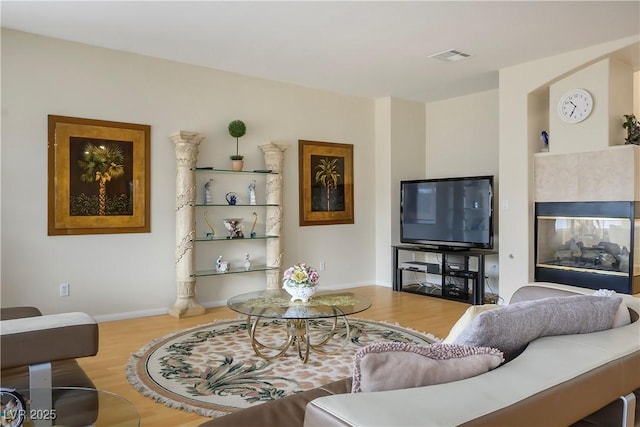 living area featuring a tiled fireplace, wood finished floors, visible vents, and baseboards