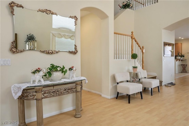 sitting room featuring stairway, arched walkways, plenty of natural light, and light wood-style flooring