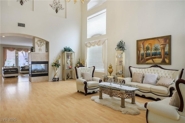 living area featuring arched walkways, a high ceiling, wood finished floors, visible vents, and a multi sided fireplace